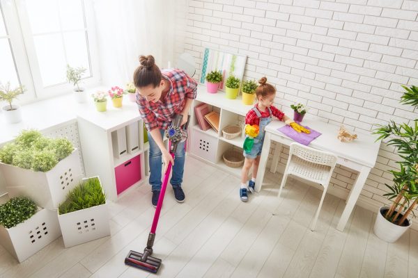 woman vacuuming the floor while girl is cleaning the table