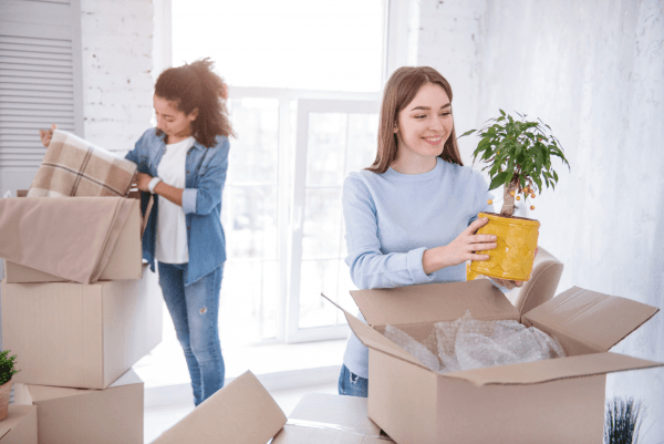 a woman placing a plant inside a cardboard box while she is packing