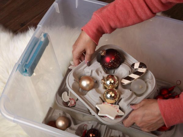 a woman in a sweater placing the holiday ornaments inside a plastic storage box