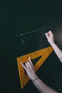Someone doing calculations on a chalkboard with a yellow ruler